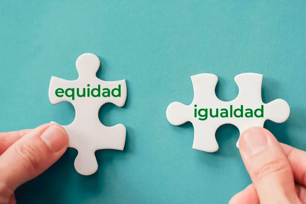 Dos manos sostienen dos piezas de rompecabezas blancas sobre un fondo turquesa. La pieza de la izquierda tiene escrita la palabra "equidad" en verde, y la de la derecha la palabra "igualdad". Las piezas están a punto de ser unidas.