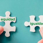 Dos manos sostienen dos piezas de rompecabezas blancas sobre un fondo turquesa. La pieza de la izquierda tiene escrita la palabra "equidad" en verde, y la de la derecha la palabra "igualdad". Las piezas están a punto de ser unidas.